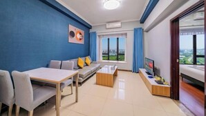 A modern living room with a blue accent wall, a sofa, a dining table, and a TV. - Angda Pazhou Apartment (Guangzhou Pazhou International Exhibition Center) (Guangzhou)