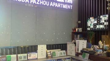 Ein Empfangsschalter mit einem Schild für Angda Pazhou Apartment, eine Broschüre zur Information und ein Bildschirm, der Zimmerauswahlmöglichkeiten anzeigt.