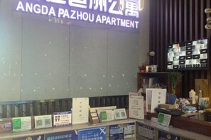 Een receptiebalie met een bordje voor Angda Pazhou Apartment, een selectie informatiemapjes en een digitaal scherm dat kameropties toont.