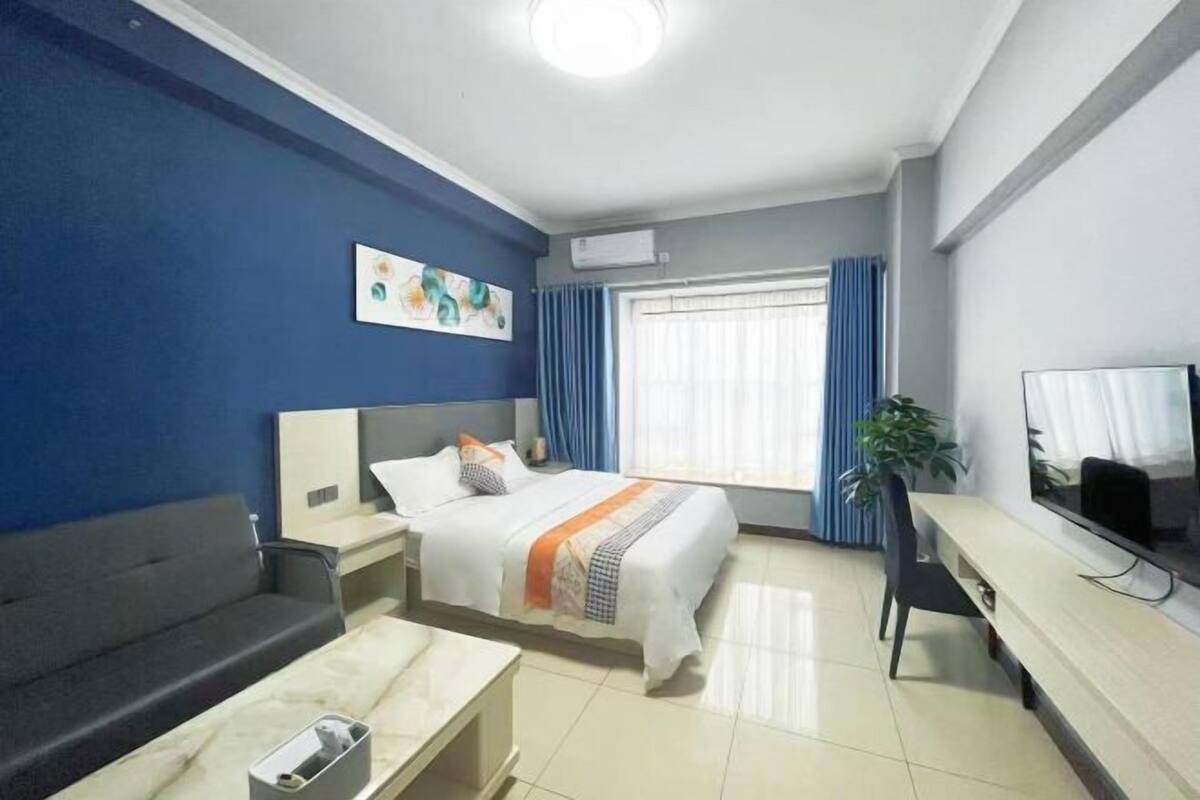 Habitació d'hotel amb llit, escriptori, cadira, televisió i finestra amb cortines.