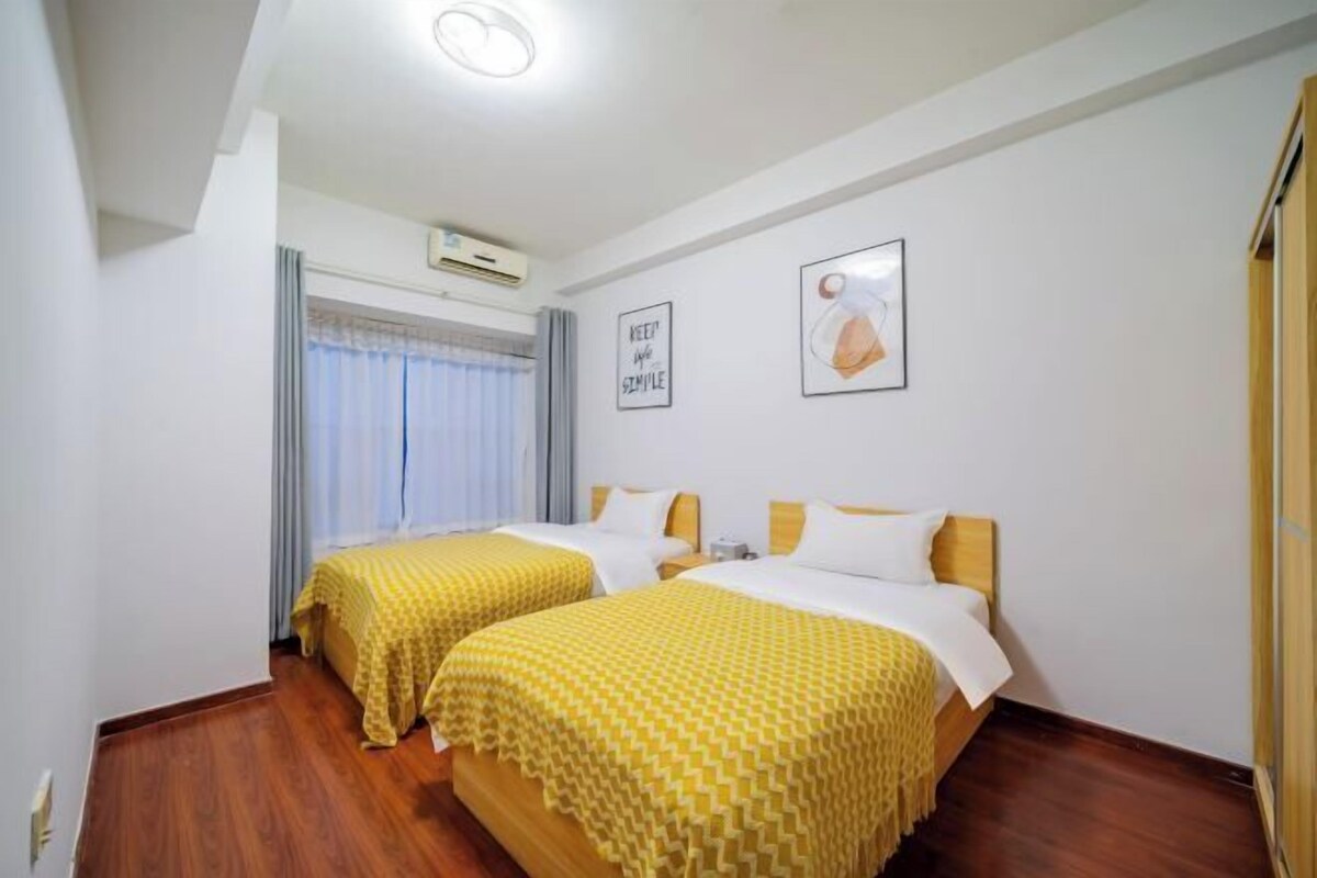 A hotel room with two beds, a window with curtains, an air conditioning unit, and a framed picture on the wall.