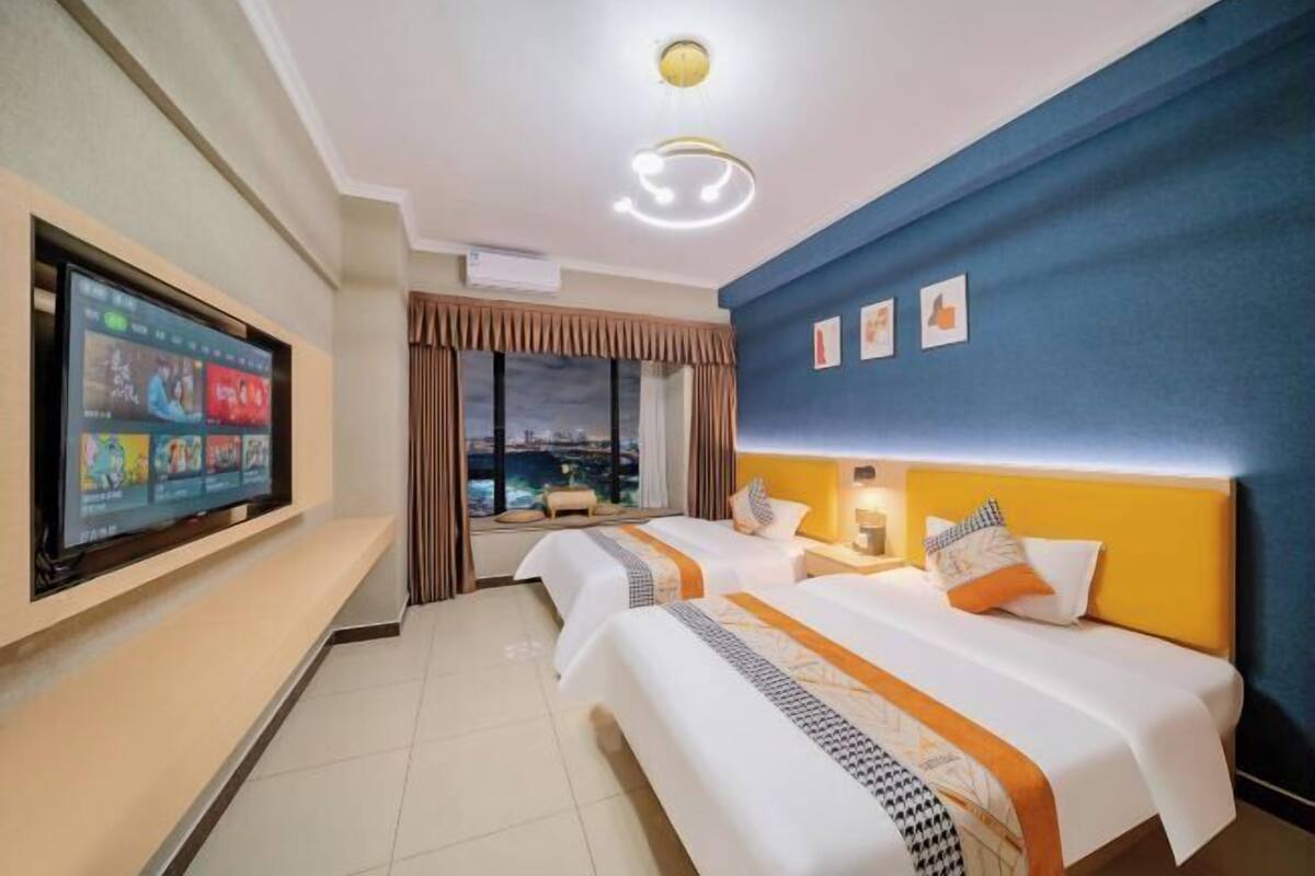 Habitació d'hotel amb dos llits, televisió penjada a la paret, vista a la ciutat i una paret d'accent blau.
