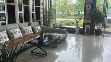 A modern hotel lobby with a curved sofa, a glass coffee table, and potted plants.