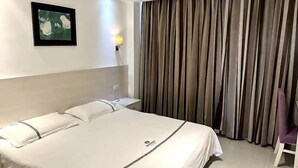 A hotel room with a bed, a nightstand, a wall-mounted light, a framed picture, and a curtain.