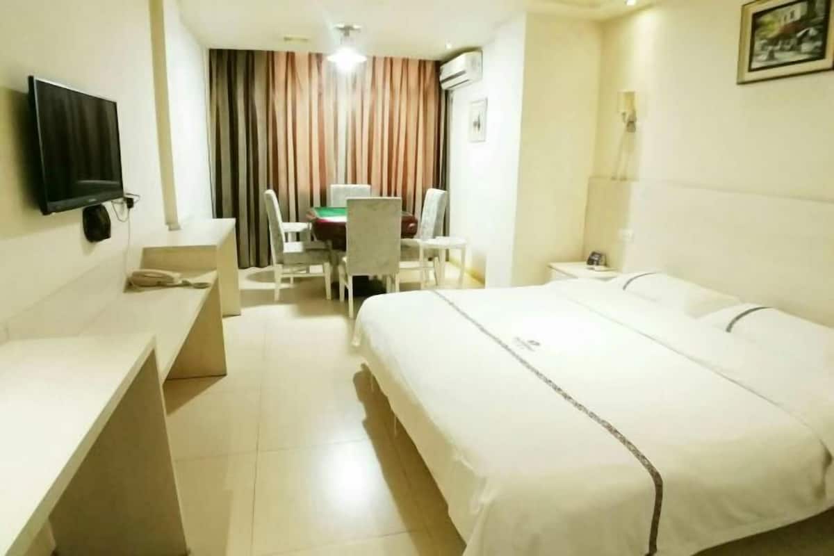 A hotel room with a bed, a desk, a chair, a television, and a dining table.