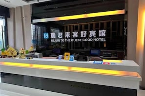 Un mostrador de recepción de hotel con un cartel en un idioma extranjero, una pantalla digital y algunos objetos sobre el mostrador.