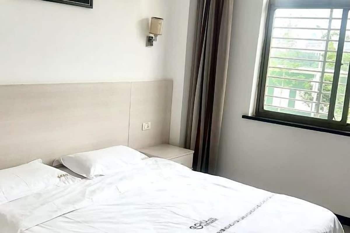 A hotel room with a bed, a nightstand, a wall-mounted light, and a window with curtains.