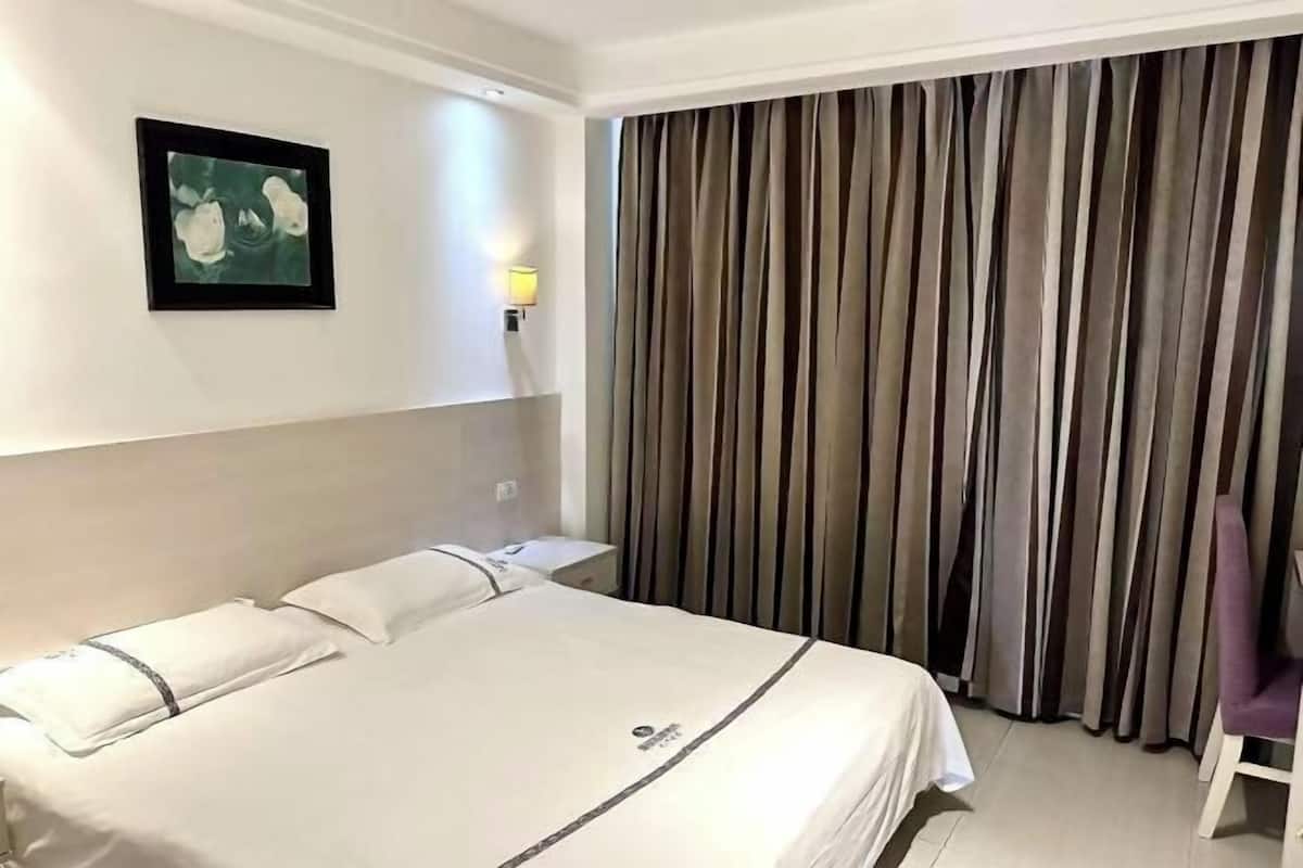 A hotel room with a bed, a nightstand, a wall-mounted lamp, a framed picture, and a curtain.