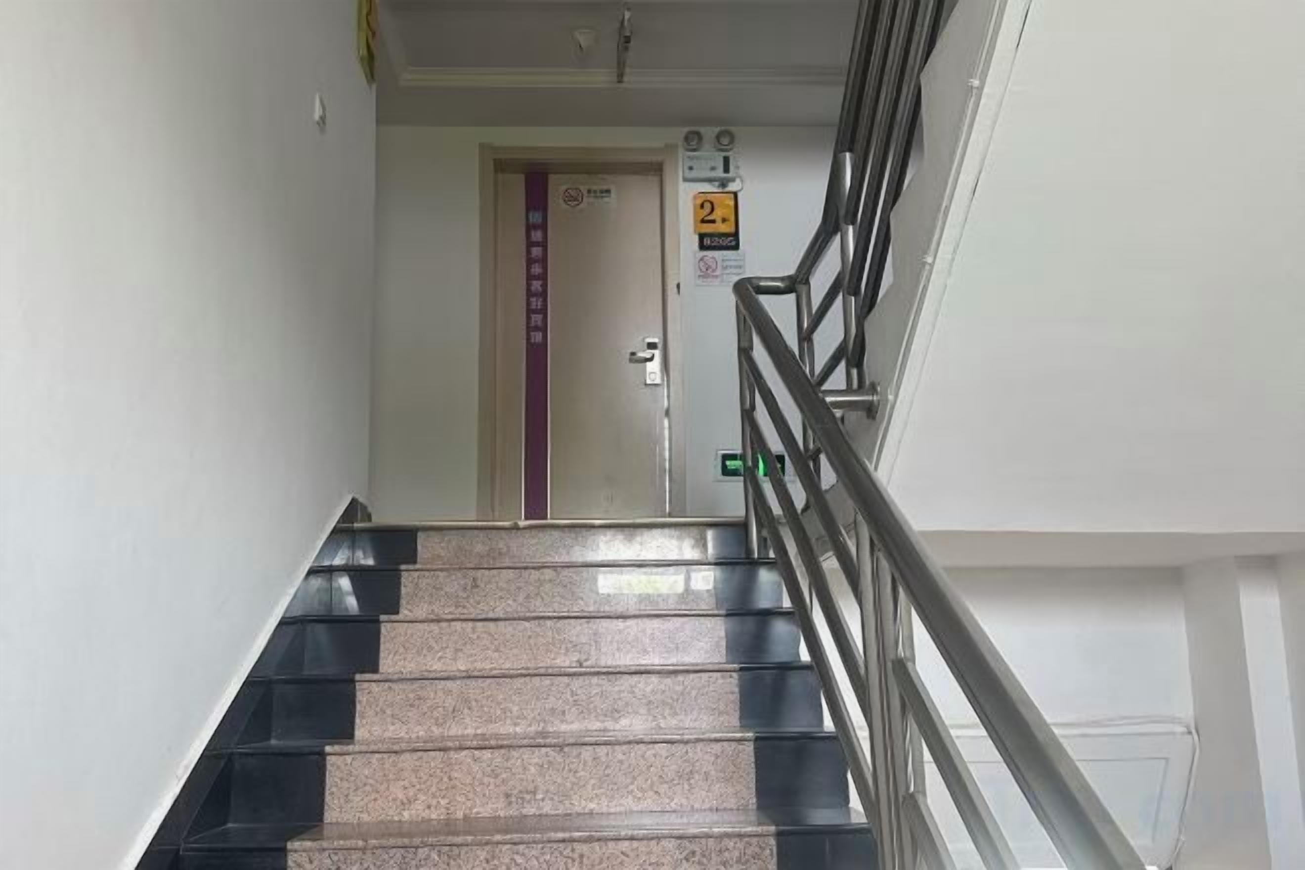 Un escalier muni d’une rampe, menant à une porte sur laquelle est apposée une plaque indiquant qu’il donne accès au deuxième étage.