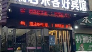 A hotel entrance with a neon sign, glass doors, and a parking sign.