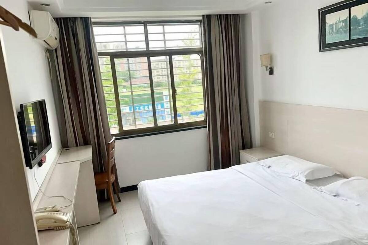 A hotel room with a bed, a desk, a chair, a TV, and a window with curtains.