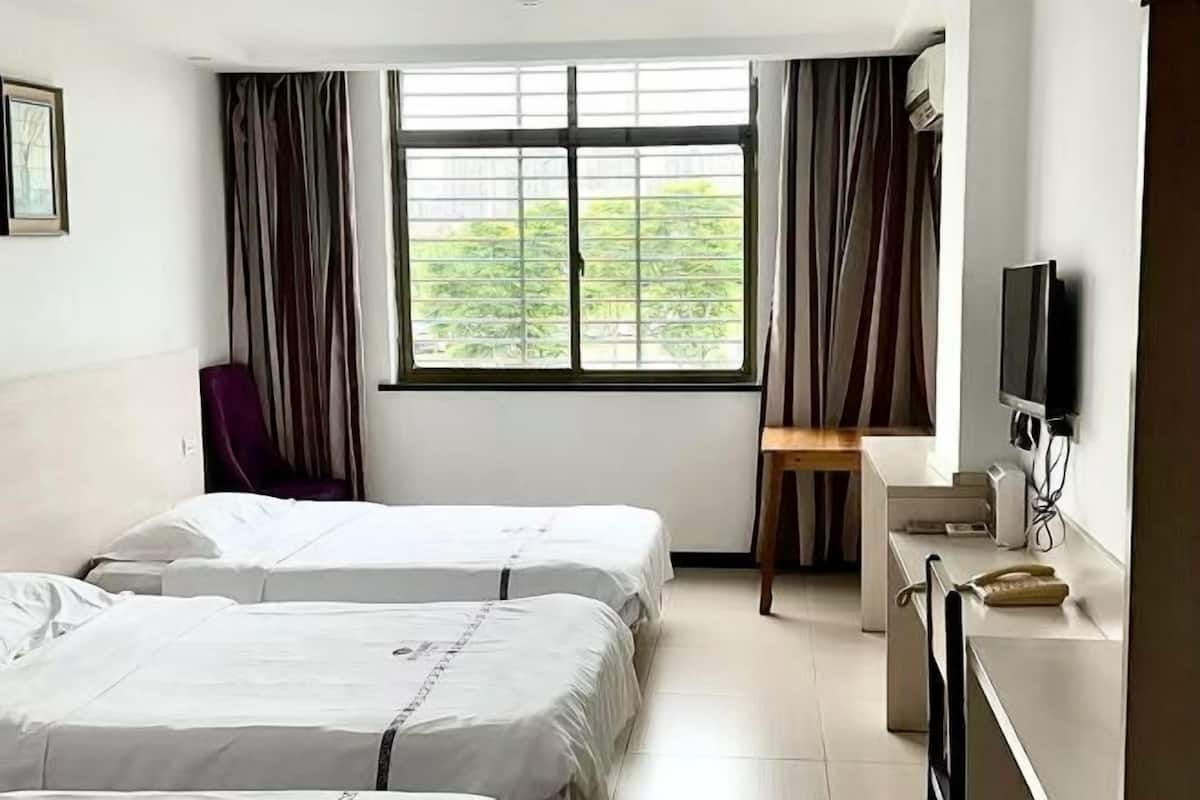 A hotel room with two beds, a desk, a chair, a TV, and a window with curtains.