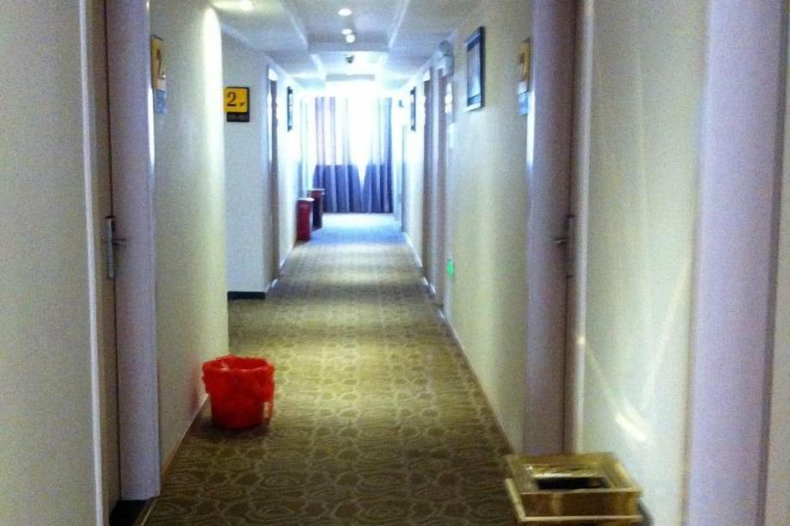 A hotel hallway with doors on both sides, a carpeted floor, and a trash bin in the center.