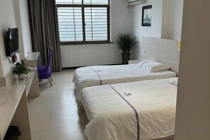 Een hotelkamer met twee bedden, een bureau, een stoel, een televisie en een raam met gordijnen.