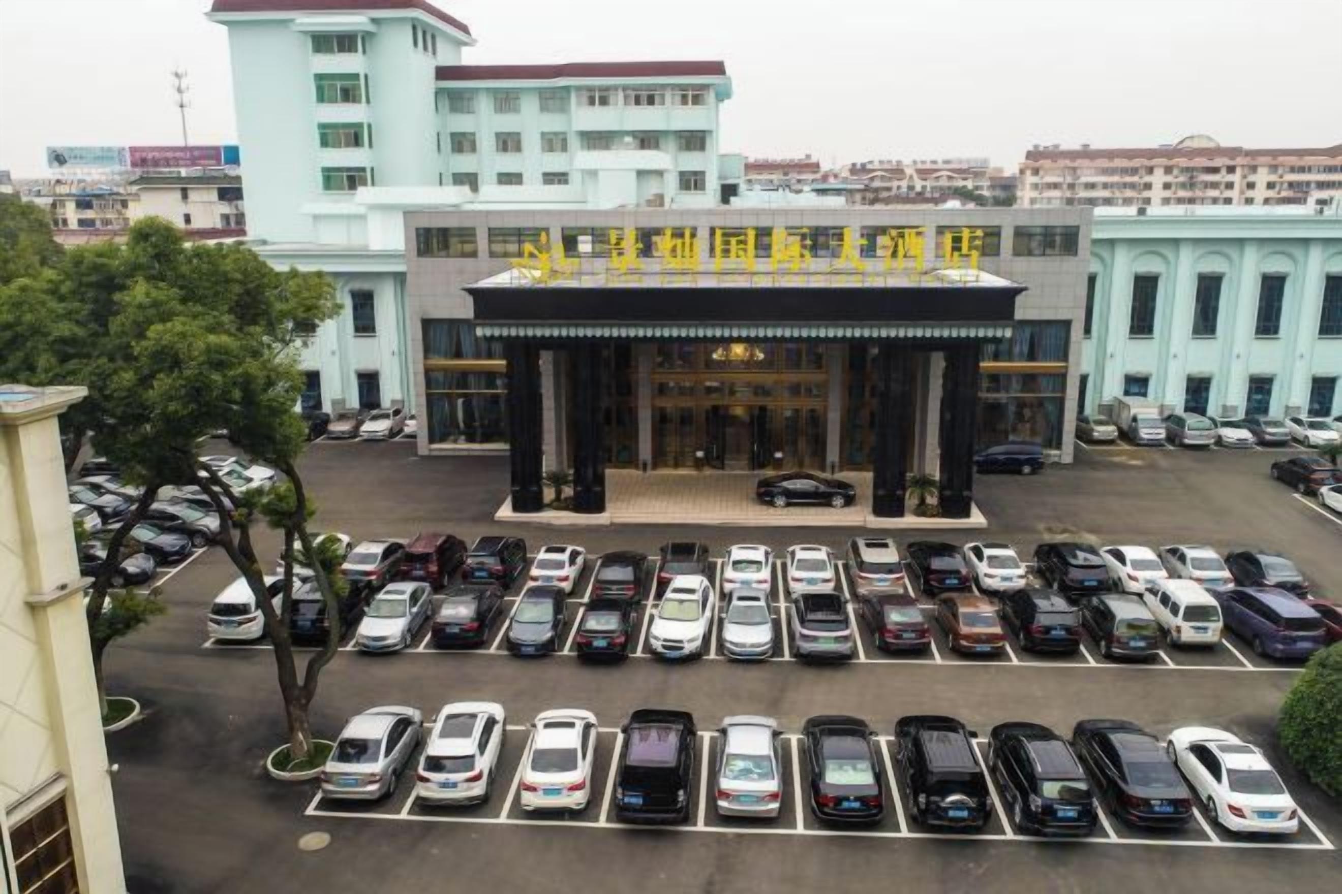 A hotel with a parking lot full of cars, a large entrance with columns, and a building with multiple floors in the background.