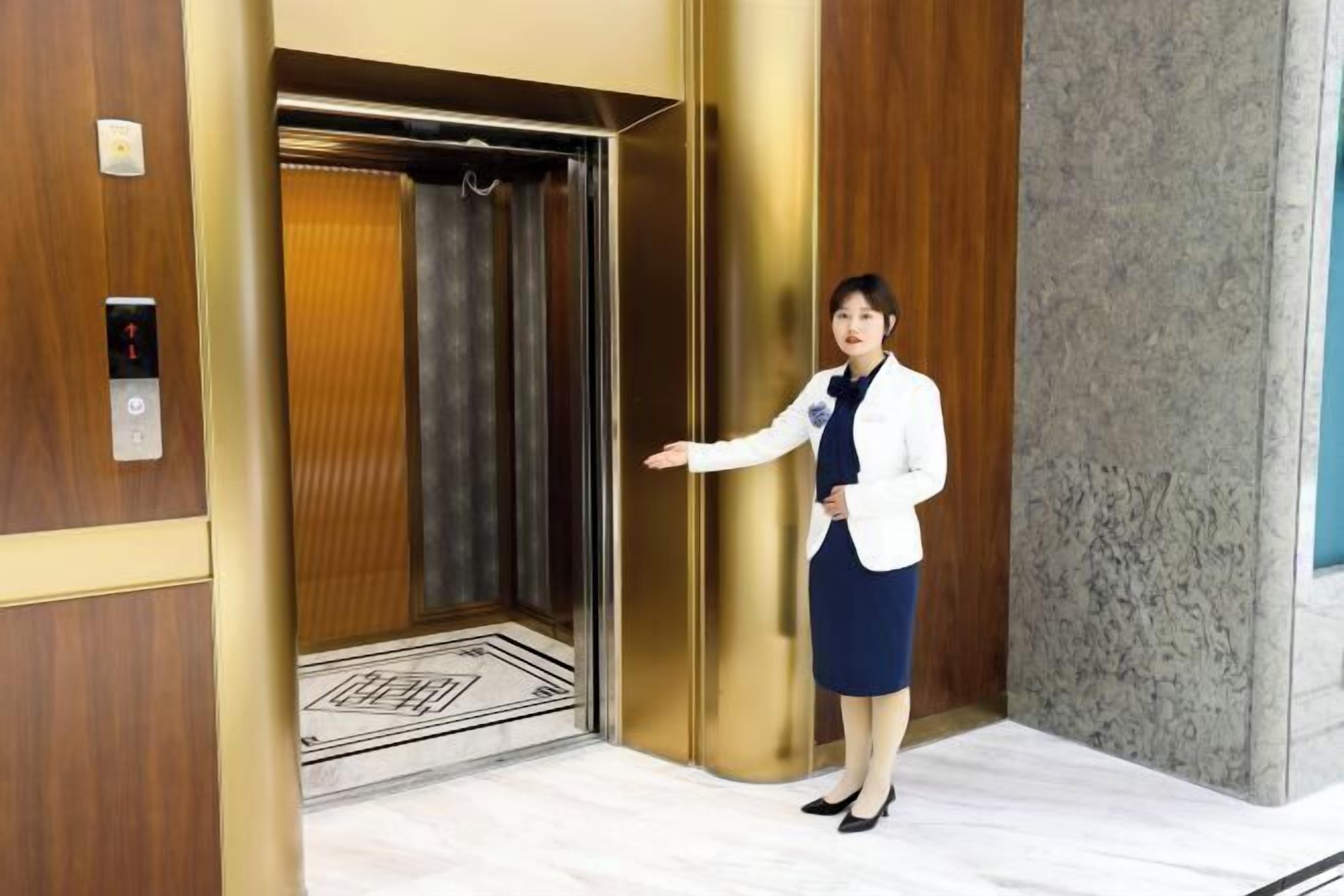 An elevator interior with a woman standing by the door, a control panel, and a patterned floor.