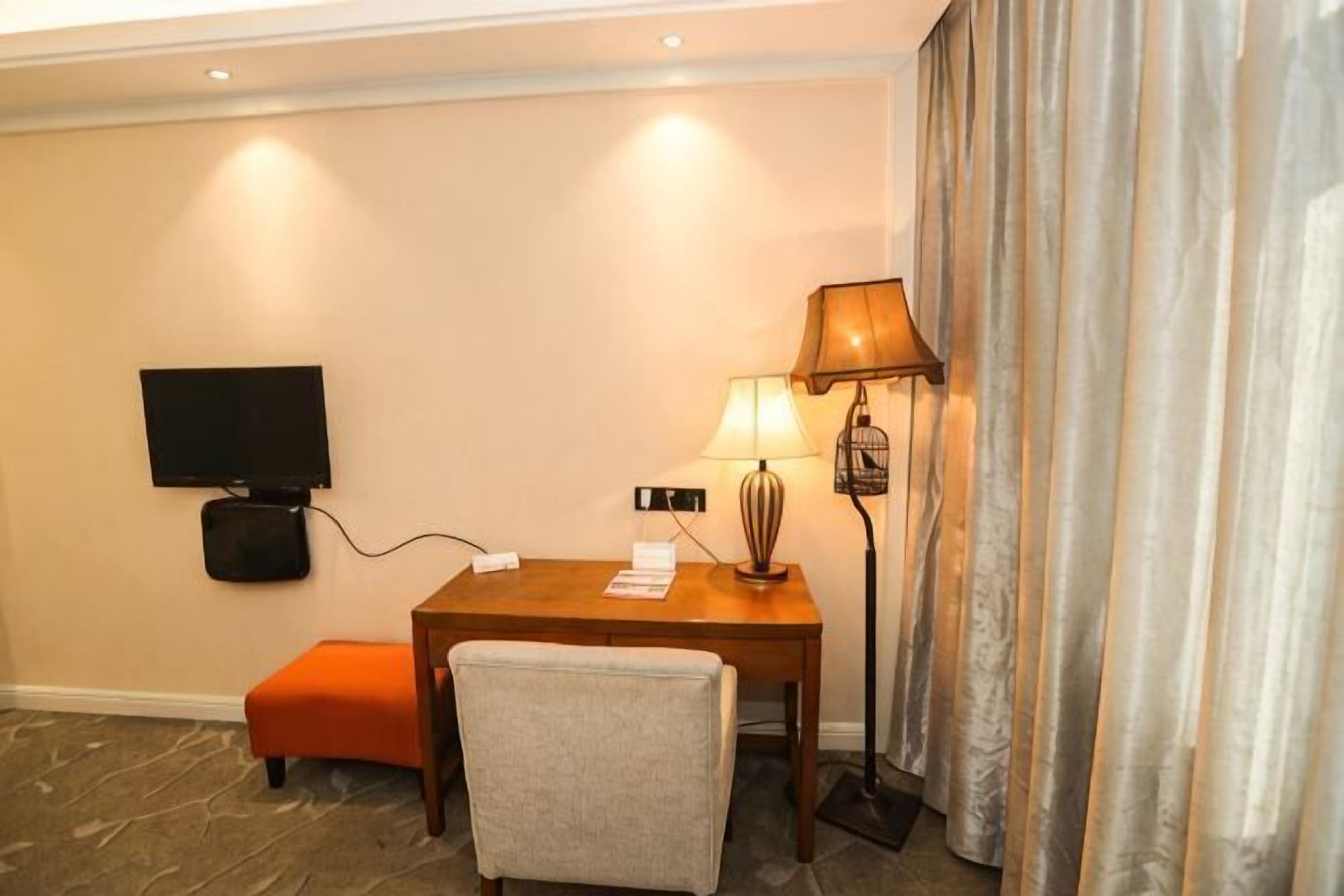 Una habitación de hotel con televisión, un escritorio con lámpara, un reposapiés y una silla.
