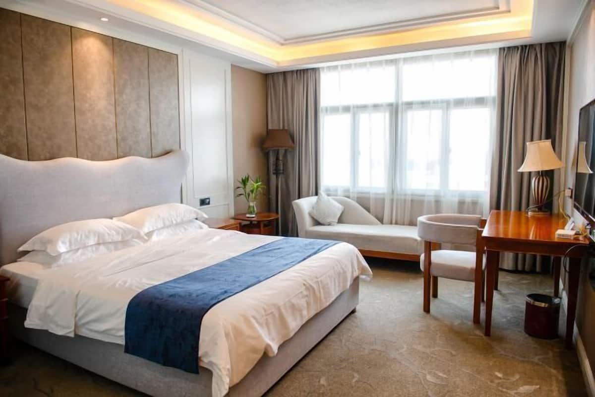 Une chambre d’hôtel avec un grand lit, un bureau, une chaise, une télévision et une fenêtre avec des rideaux.
