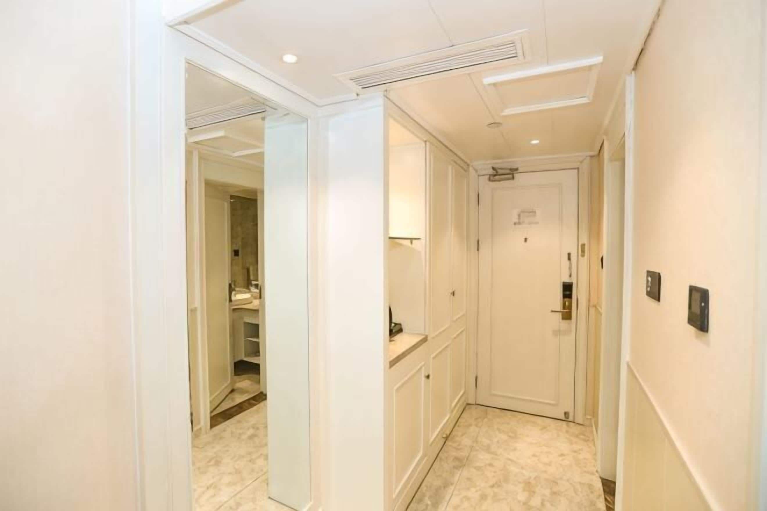 A narrow hallway with a door at the end, a mirror on the left, and a light fixture on the ceiling.