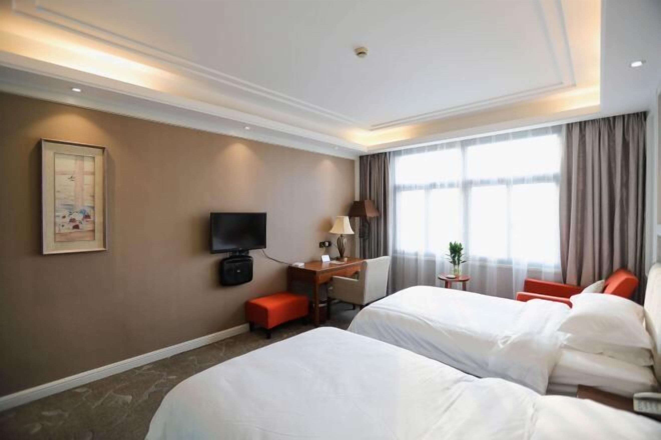 A hotel room with two beds, a desk with a chair, a television, a window with curtains, and a framed picture on the wall.