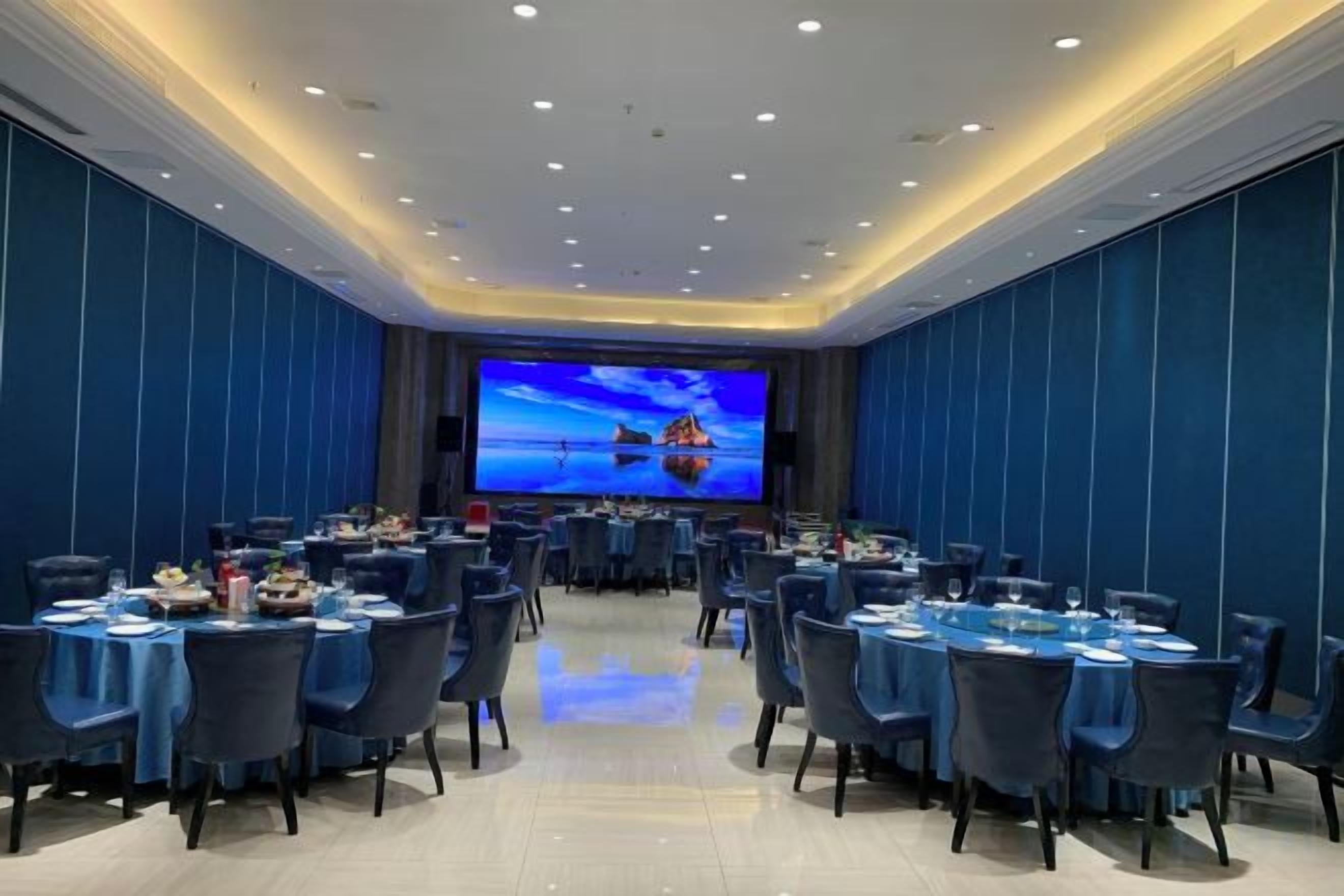 A conference room with round tables, chairs, and a large screen displaying a scenic image.