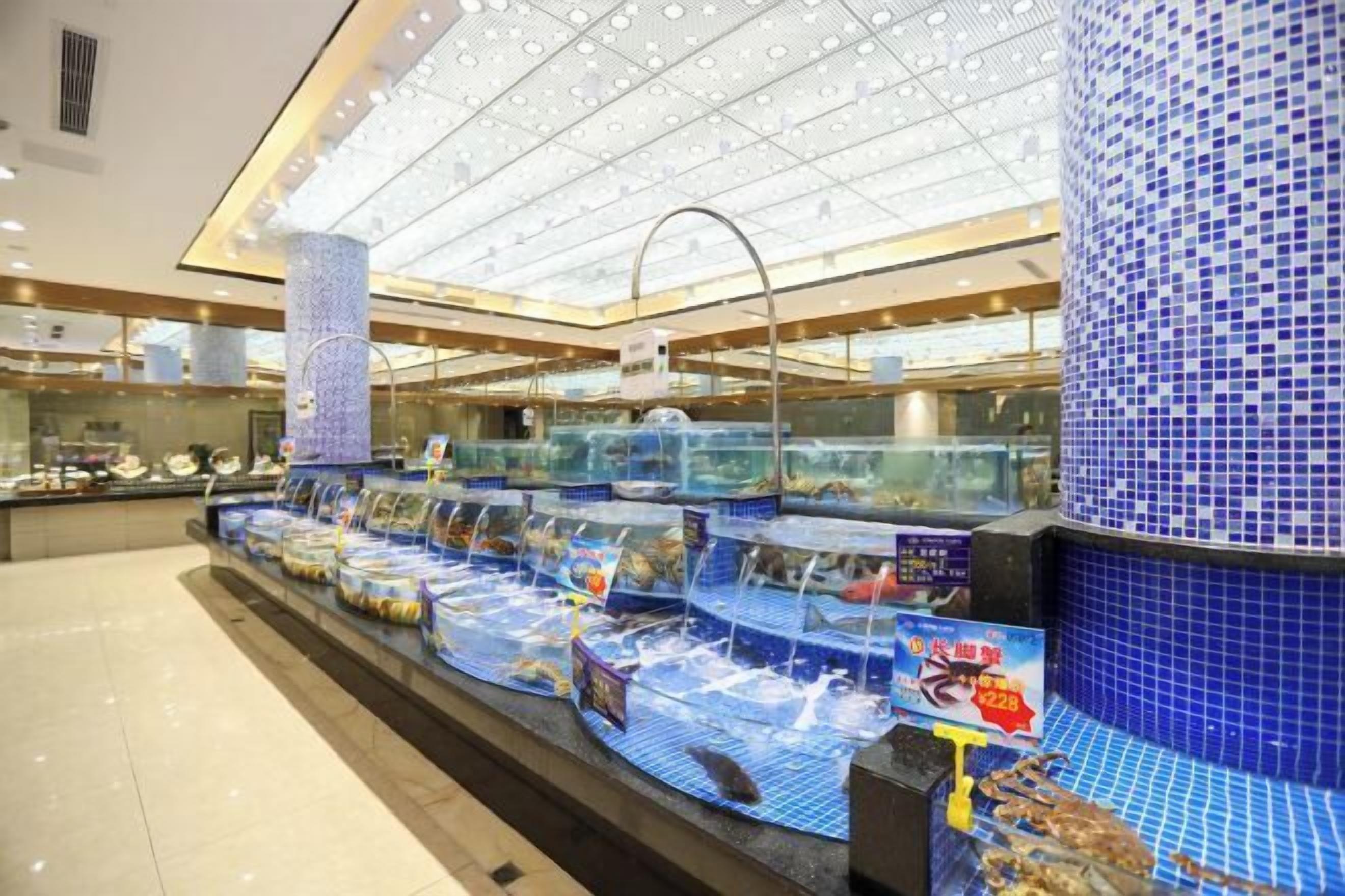 Exposição de frutos do mar com tanques e placas, teto azulejado e balcão de vidro.