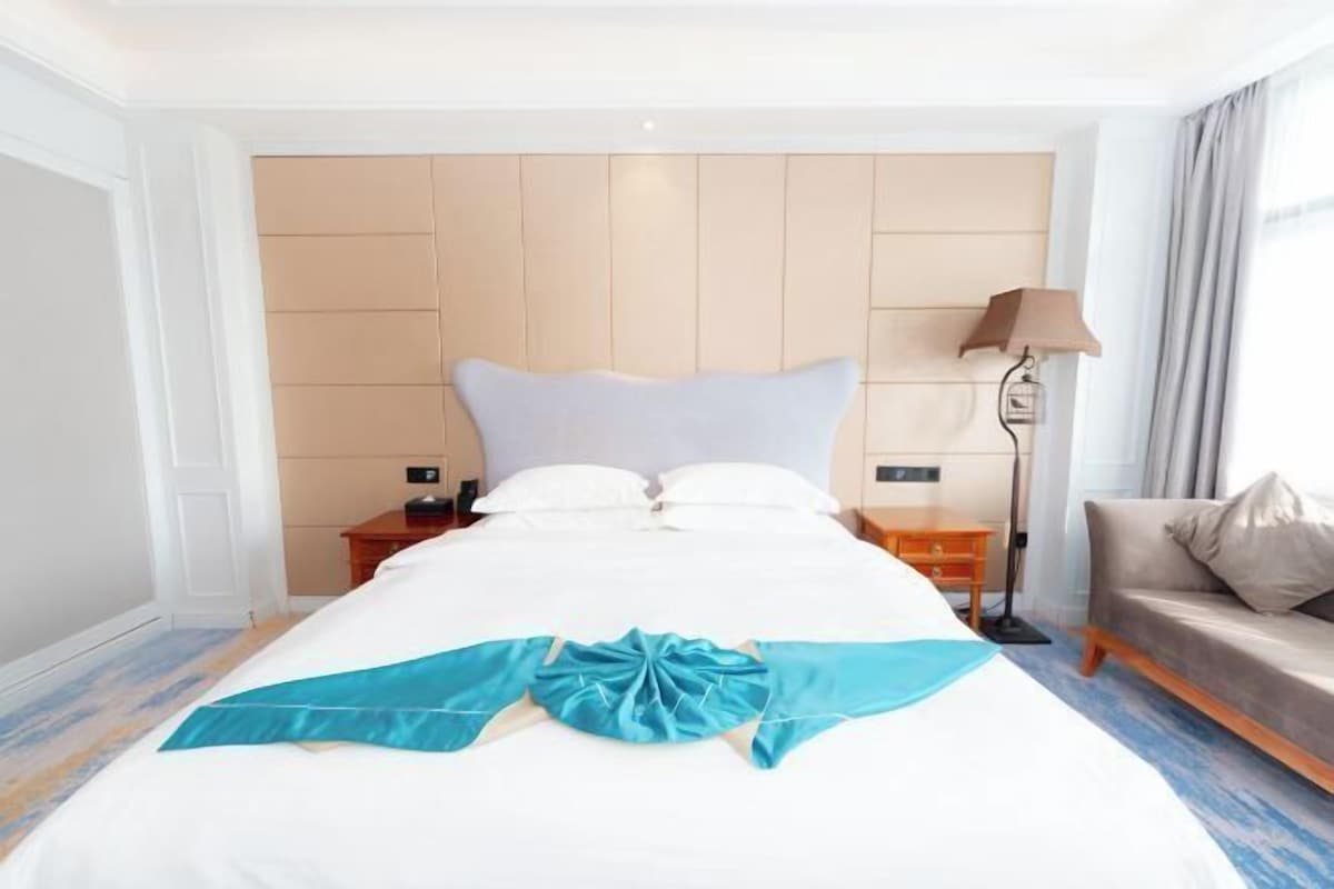 Une chambre d’hôtel avec un lit, une table de chevet, une lampe, un canapé et une fenêtre avec des rideaux.