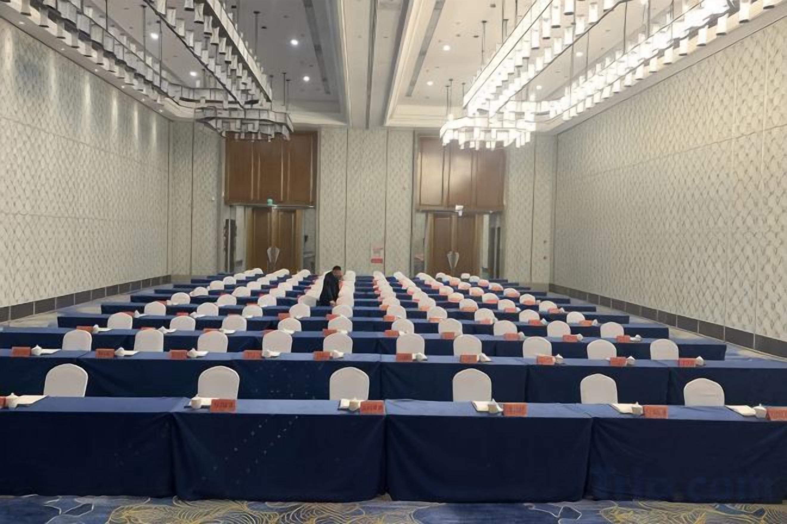 A conference room with rows of tables and chairs, a chandelier, and a patterned wall.