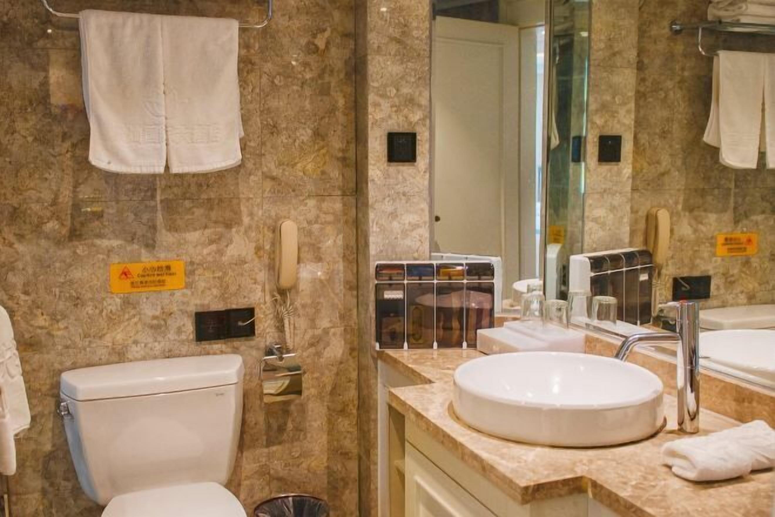 A bathroom with a marble wall, a toilet, a sink, and a mirror.