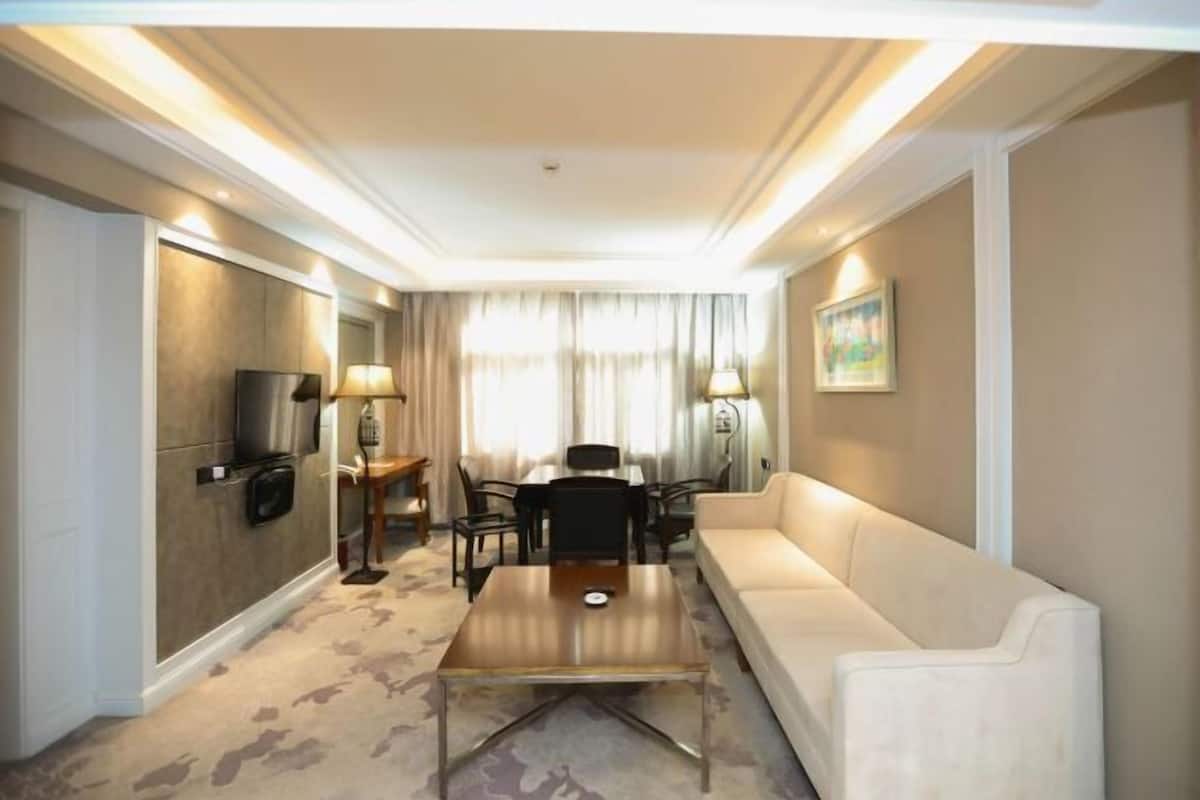 Une chambre d’hôtel avec un canapé, une table basse, une télévision, un bureau avec des chaises et un tableau au mur.