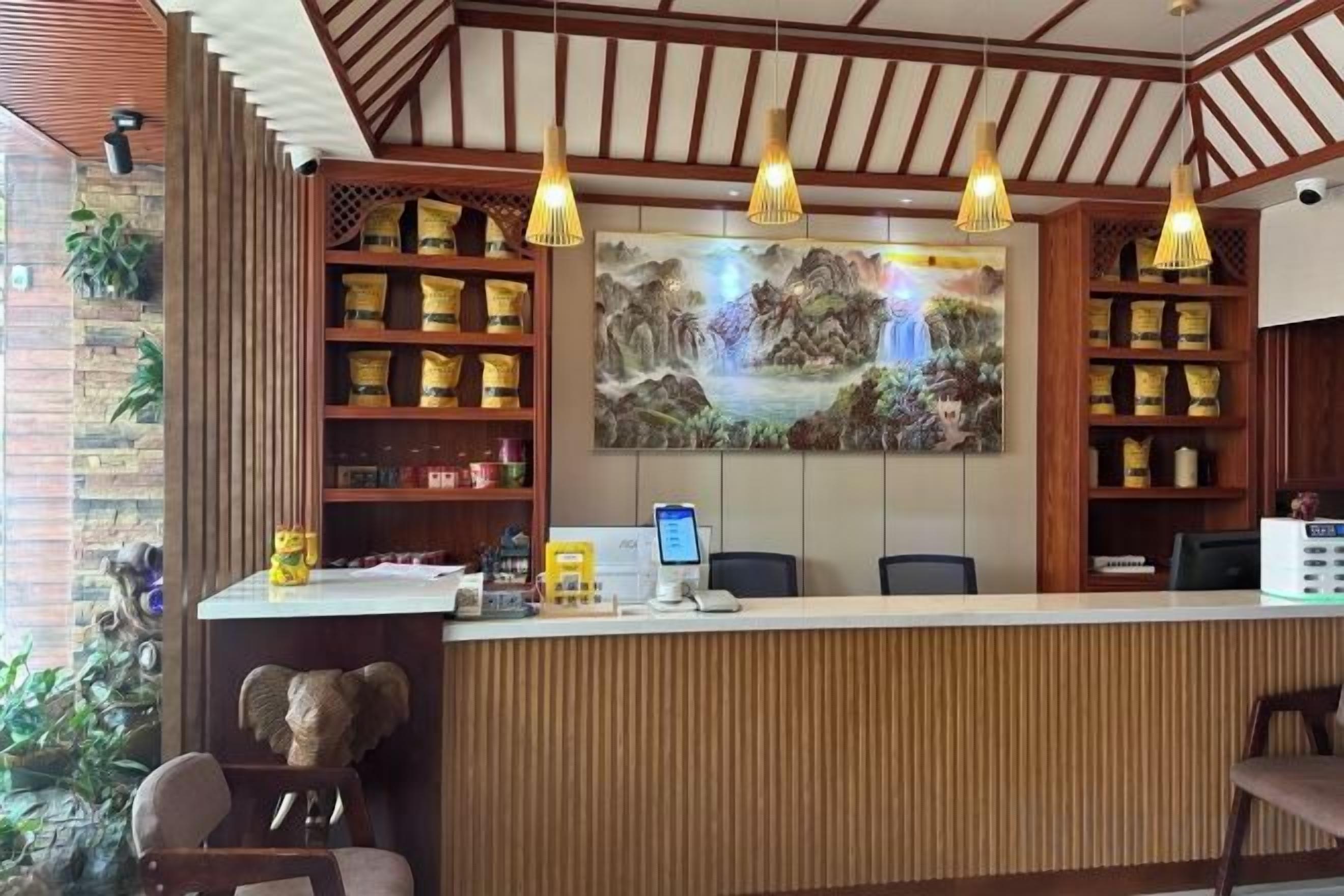 A reception desk with a wooden finish, a large painting above it, and a shelf with various items.