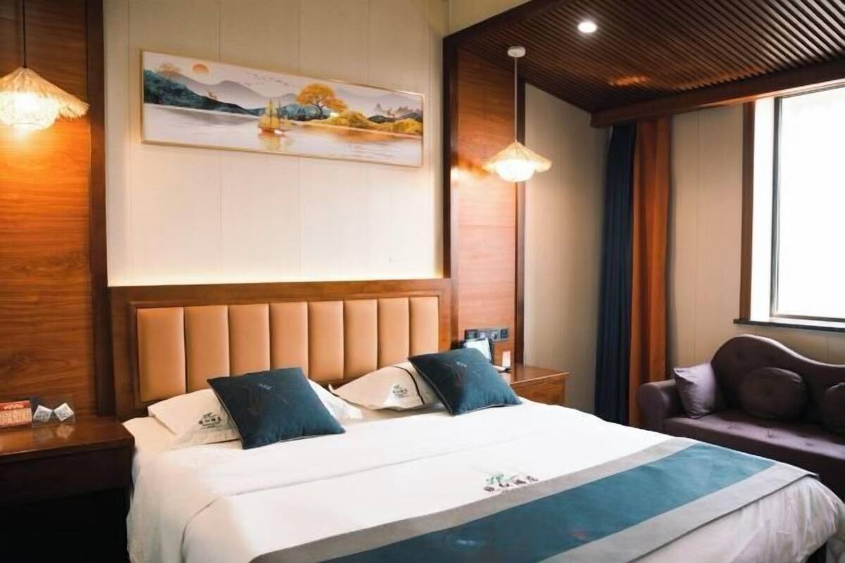Een hotelkamer met een bed, nachtkastje, een schilderij aan de muur en een raam met gordijnen.