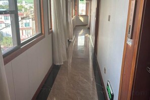 A corridor with a tiled floor, a door on the right, and a window on the left. - Jinggu Xiaohong Hotel (Jinggu)