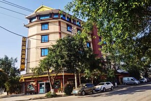 Un hôtel à plusieurs étages, doté d’une entrée imposante, d’un restaurant bien visible et d’une zone de stationnement pour les voitures.