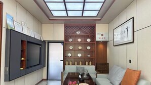 Una sala de estar moderna con un televisor montado en la pared, una mesa de comedor con un frutero y una estantería decorativa con platos.