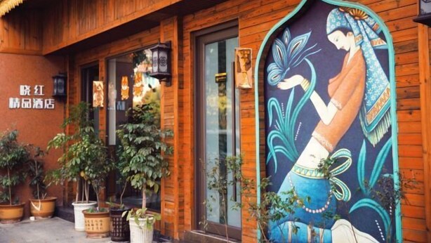 Un edificio tradicional de madera con un gran mural de una mujer sosteniendo un abanico. Hay plantas en macetas afuera y un letrero con caracteres chinos.