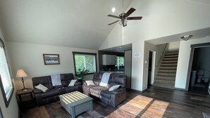 A spacious living room with a dark wood floor, a ceiling fan, a sofa set, a coffee table, and a view of the kitchen and staircase. - Cozy Getaway in Mullan (Mullan)