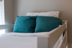 Una cama blanca con almohadones turquesa y cabecera blanca.