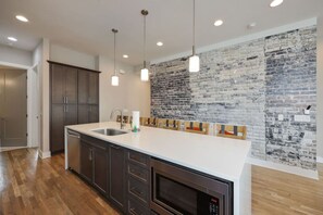 Una cocina moderna con una isla grande, gabinetes oscuros y una pared de ladrillo decorativa.