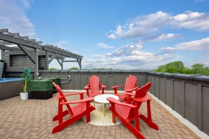 A rooftop patio with red Adirondack chairs, a small round table, and a pergola structure.