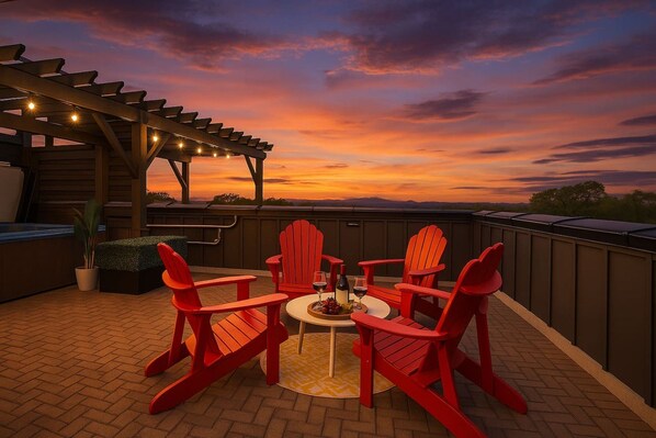 Un patio con sillas Adirondack rojas, una mesita redonda y una pérgola con luces colgantes.
