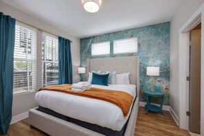 Un dormitorio moderno con una cama grande, dos lámparas de noche y vistas a la ciudad a través de las ventanas.