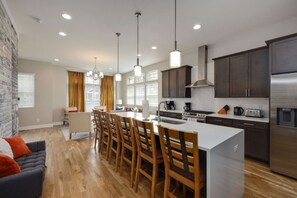 Une cuisine moderne avec un îlot central, des chaises en bois et des meubles de rangement de couleur sombre.
