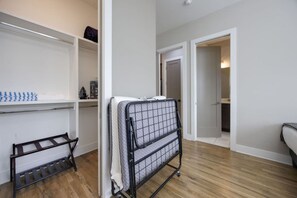 A room with a wooden floor, a metal drying rack, a mattress on a metal frame, and a white door leading to another room. - Soak & Unwind | West End Hot Tub Retreat (Nashville)