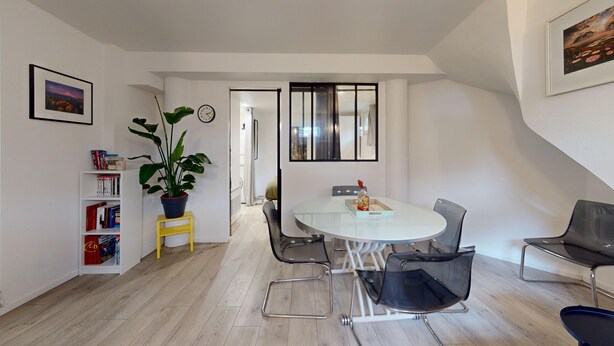 Een moderne eetruimte met een ronde tafel, stoelen en een boekenkast met boeken en een plant.