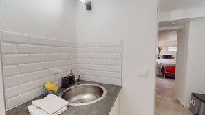 Een badkamer met een witte betegelde muur, een roestvrijstalen wastafel, een gele spons en een zwarte container met een kraan.