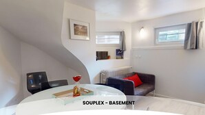 Een moderne woonkamer met een eettafel, een bank en een radiator. Er is een raam met gordijnen en een schilderij aan de muur.