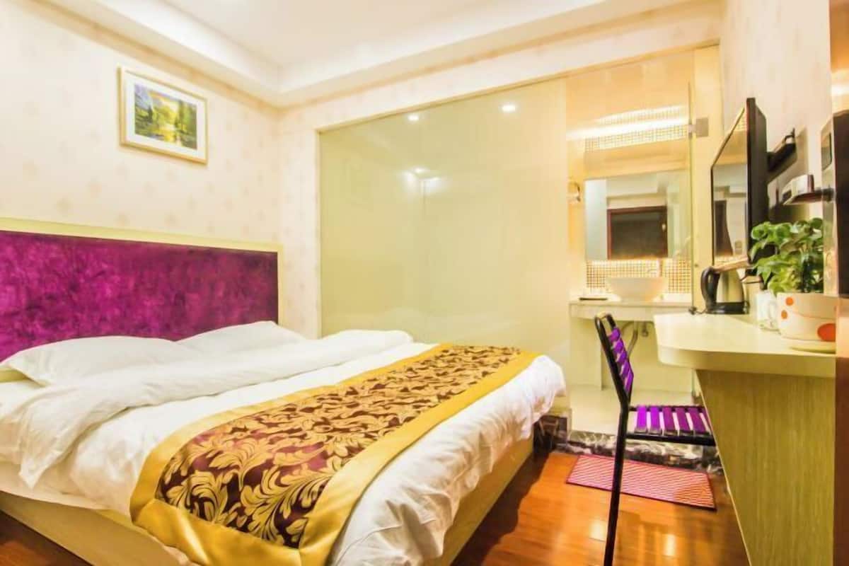 Una habitación de hotel con cama, escritorio, silla, espejo y una planta.