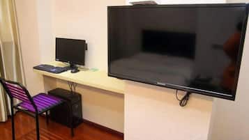 A room with a flat-screen TV mounted on the wall, a desk with a computer, and a chair.