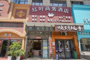 A hotel with a red signboard, a visible entrance, and a potted plant outside. - Hongye Business Hotel (Yichang)